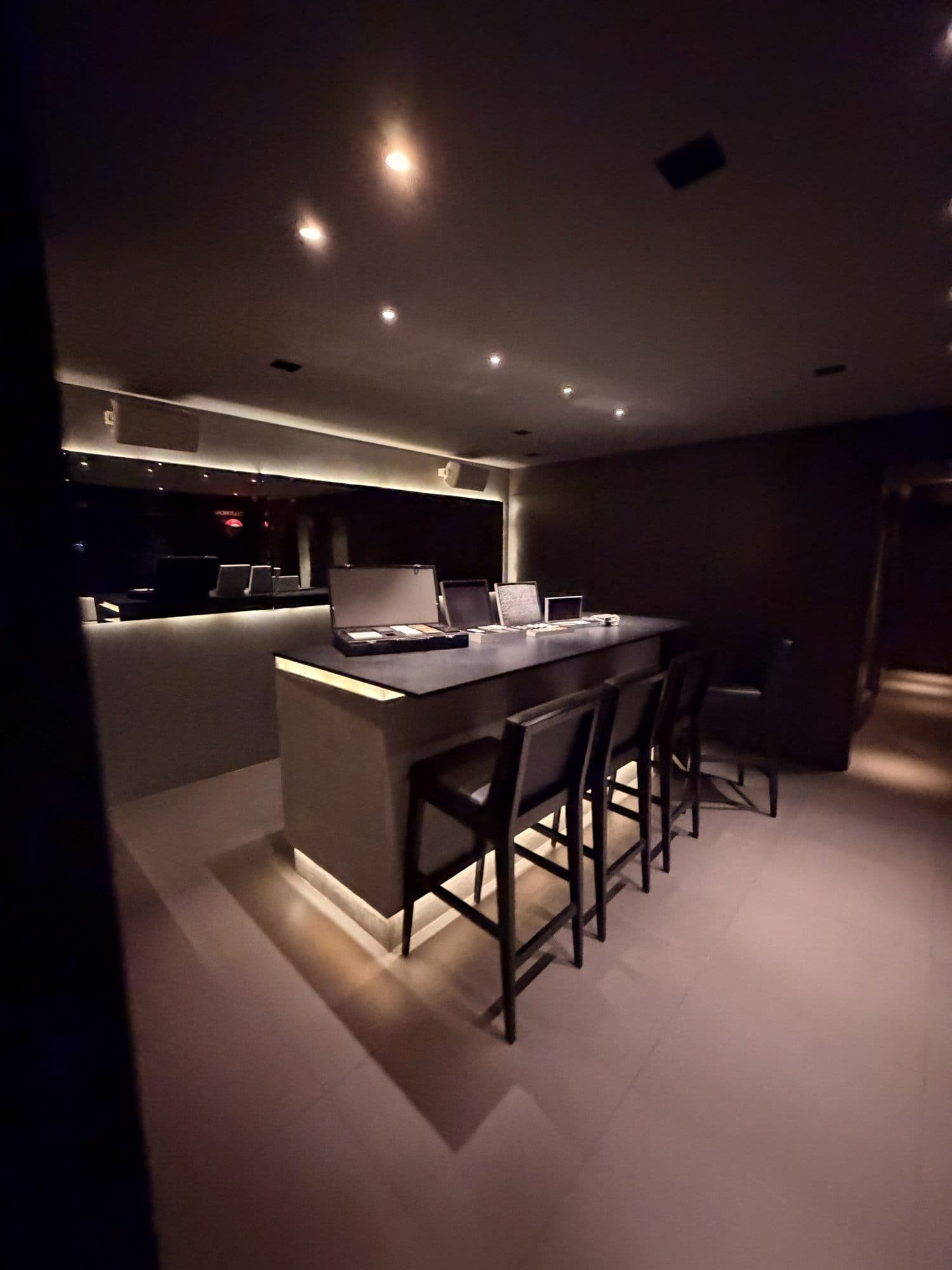 Bar residencial integrado a sala de home theater com iluminação de cena dourada e prateleiras iluminadas